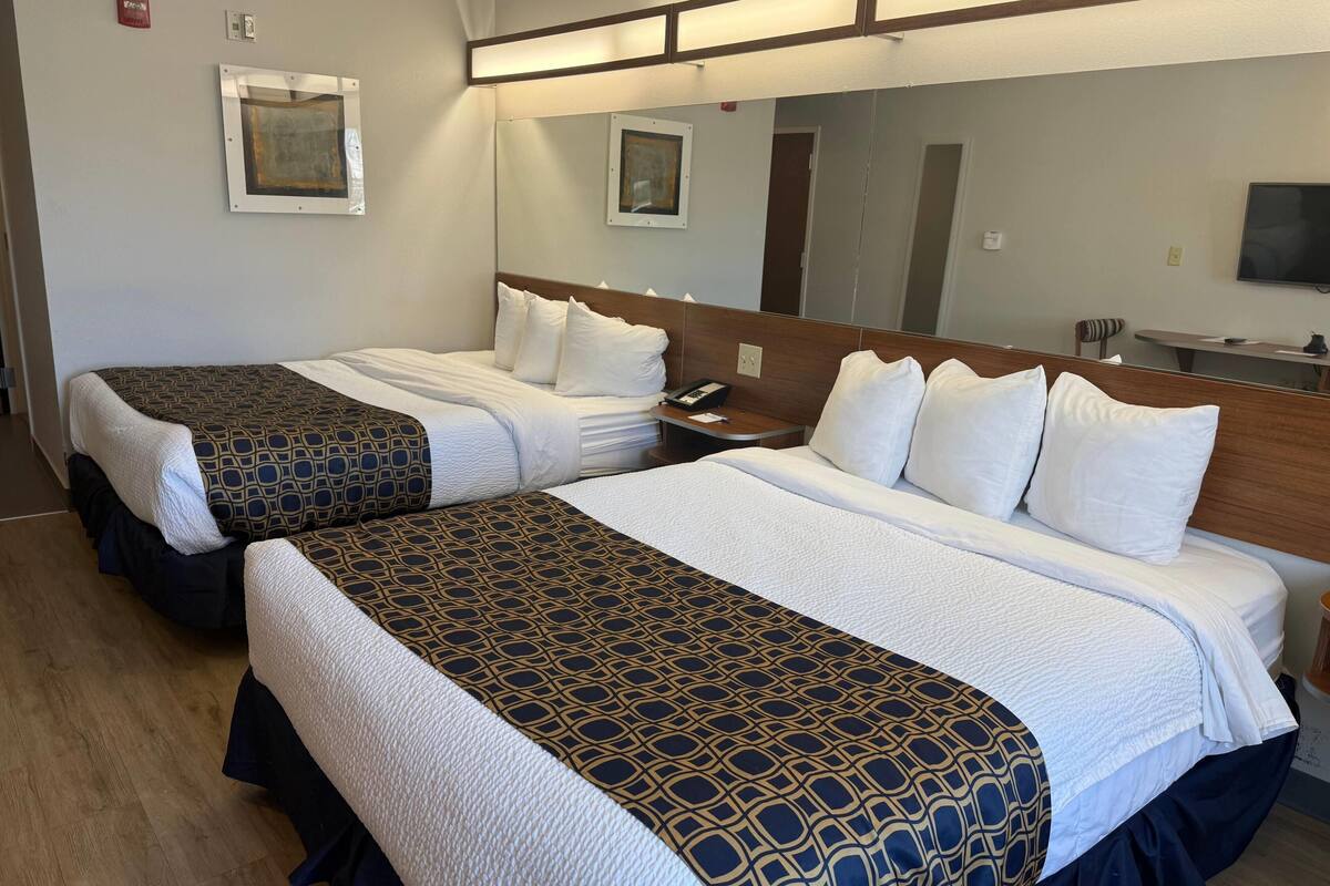 Two single beds with patterned bedspreads, a bedside table with a phone, a mirror, and a television on the wall.