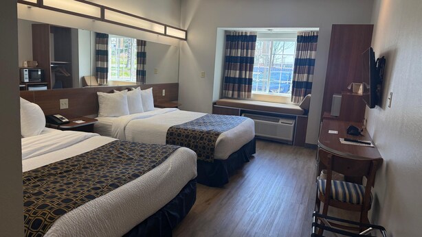 Une chambre d’hôtel avec deux lits, un bureau, une chaise, un miroir et une fenêtre avec des rideaux.