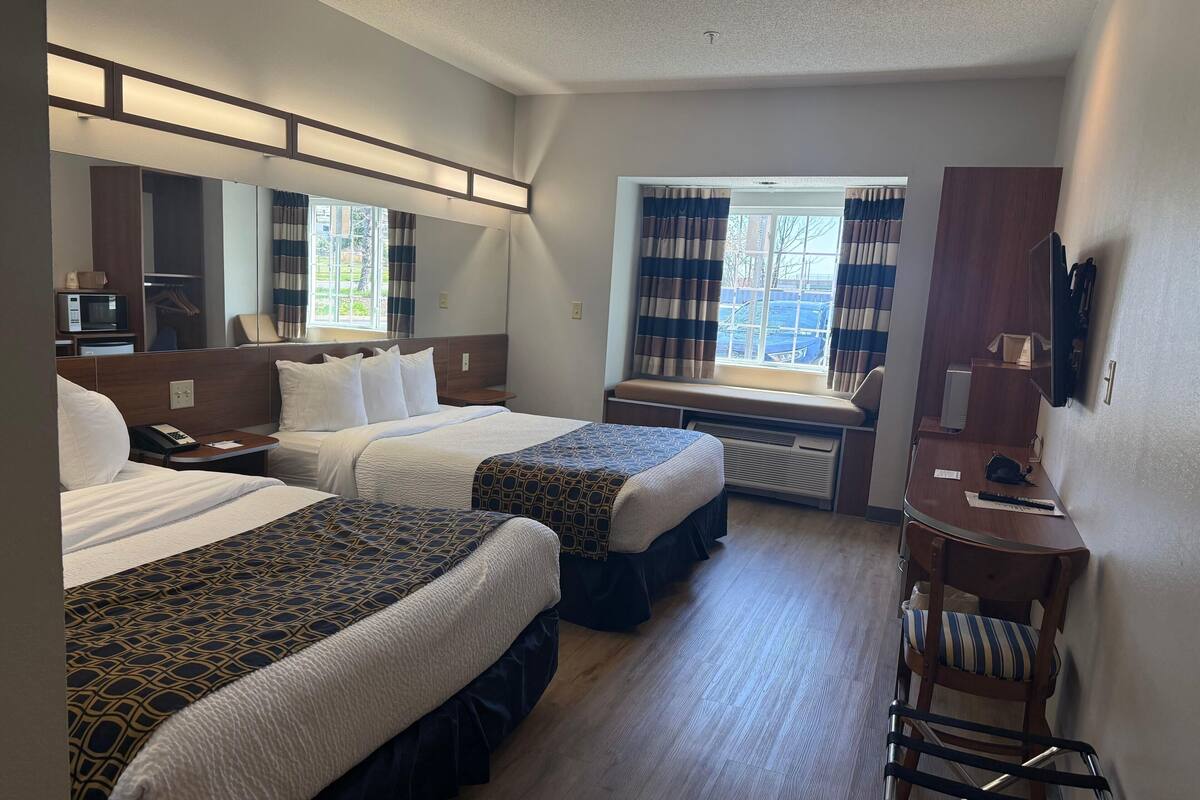 A hotel room with two beds, a desk, a chair, a mirror, and a window with curtains.