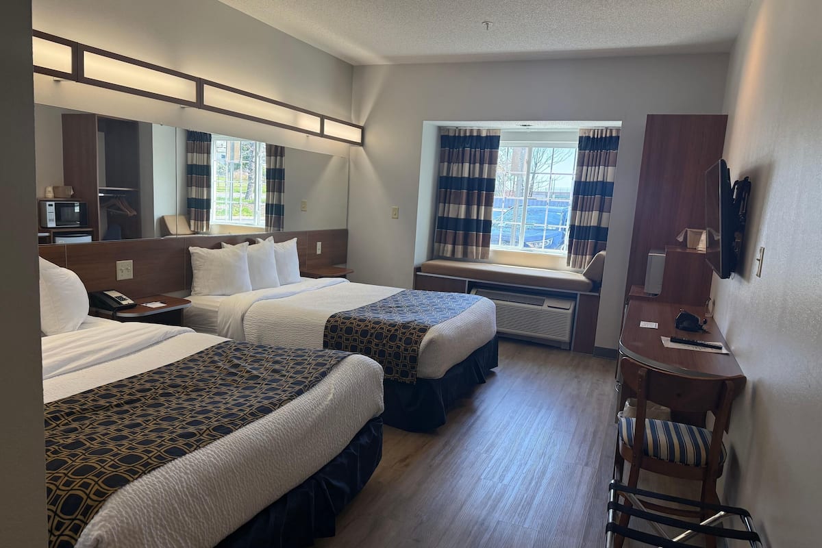 A hotel room with two beds, a desk, a chair, a mirror, and a window with curtains.