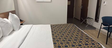 A hotel room with a bed, a chair, a desk, and a painting on the wall.