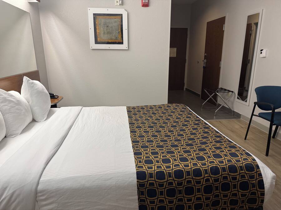 Una habitación de hotel con cama, una silla, un escritorio y un cuadro en la pared.