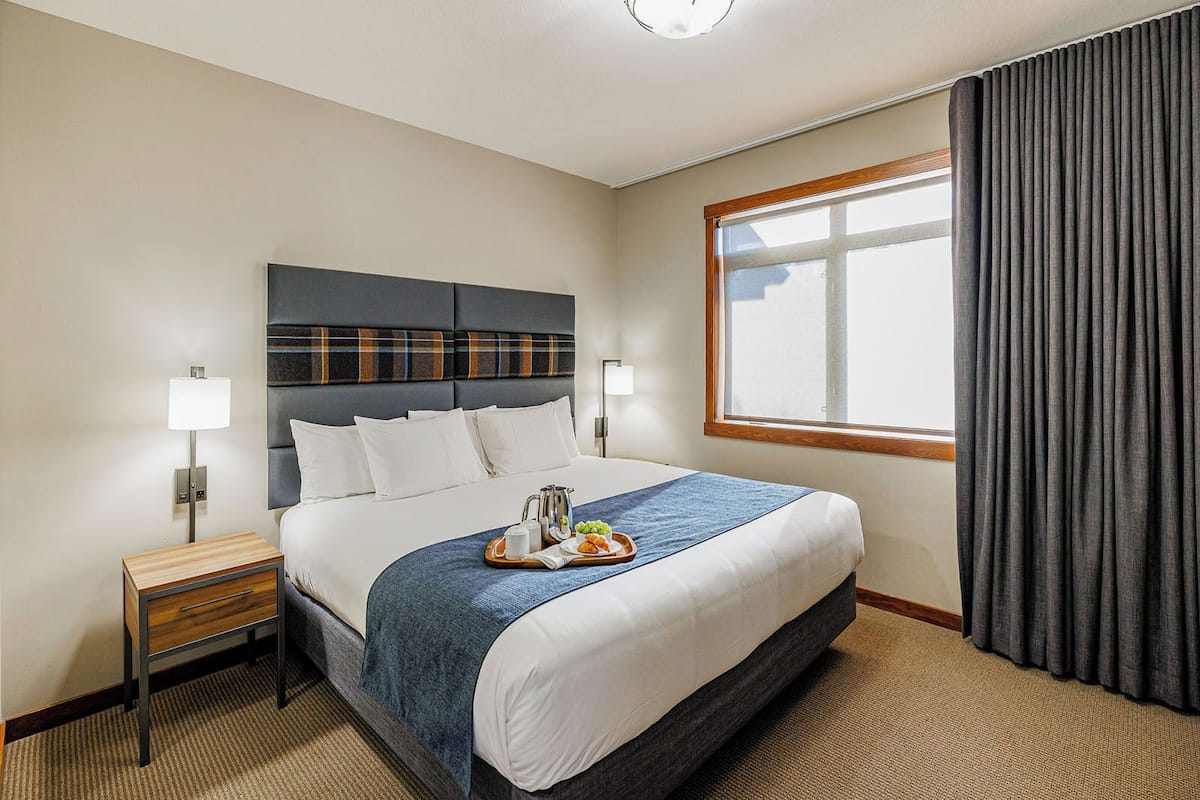 A hotel room with a bed, bedside tables, a window with curtains, and a view of the outside.