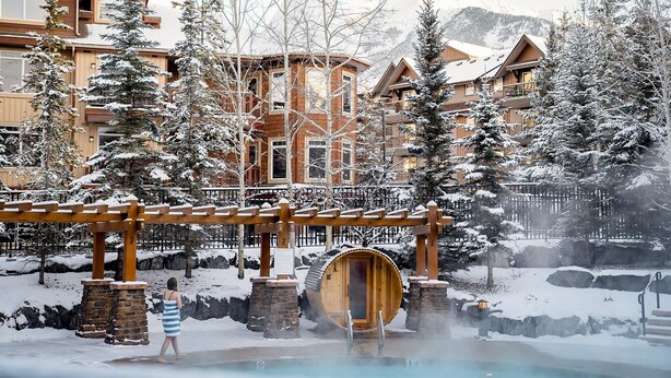 A snow-covered outdoor area with a wooden sauna, stone pillars, and a wooden pergola. - Stoneridge Mountain Resort (Canmore)