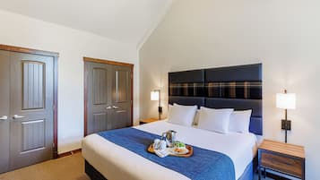 A hotel room with a large bed, a wooden nightstand, two bedside lamps, and a tray with breakfast items on the bed.