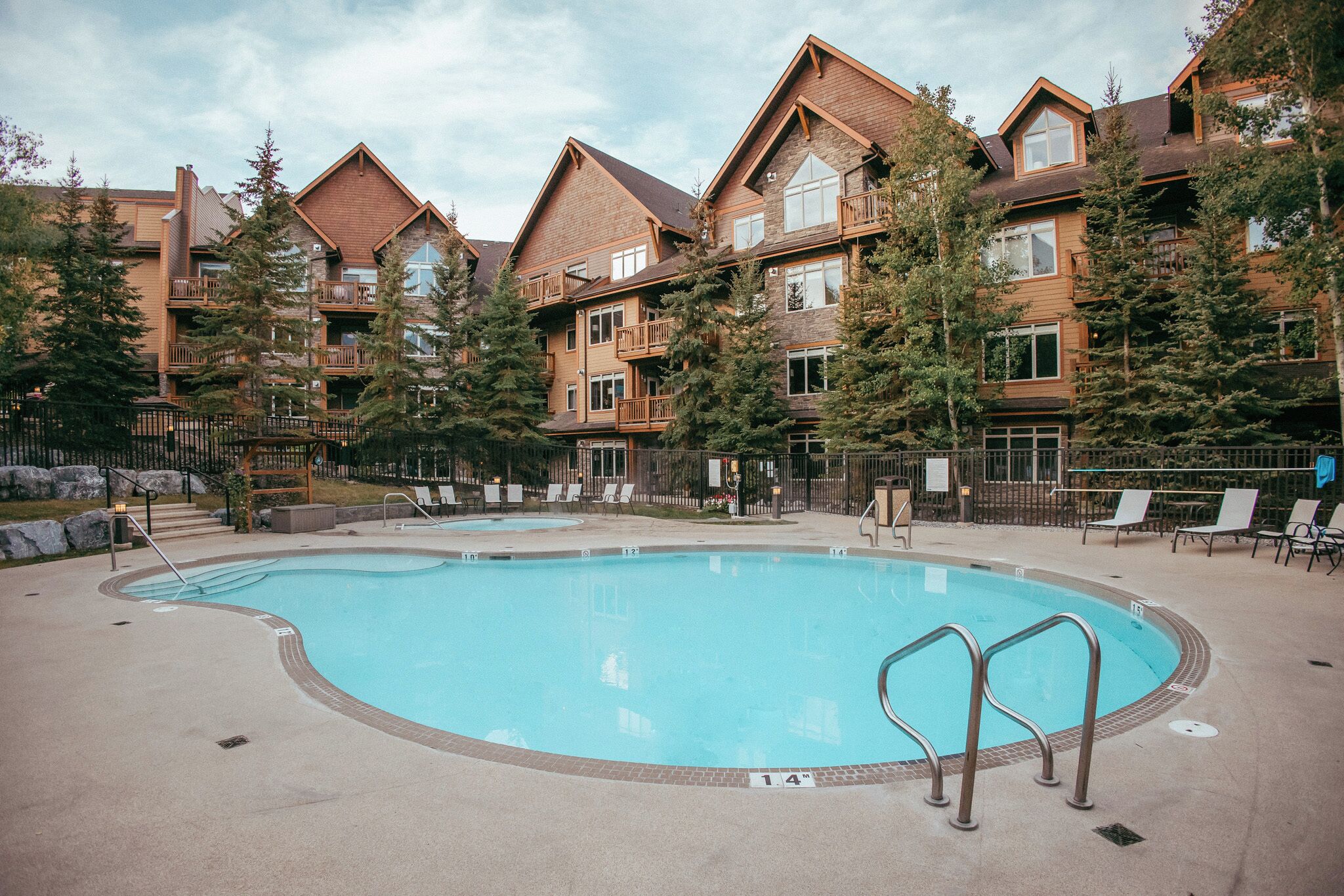 A pool area with a clear blue pool, surrounded by lounge chairs and a wooden building with balconies.