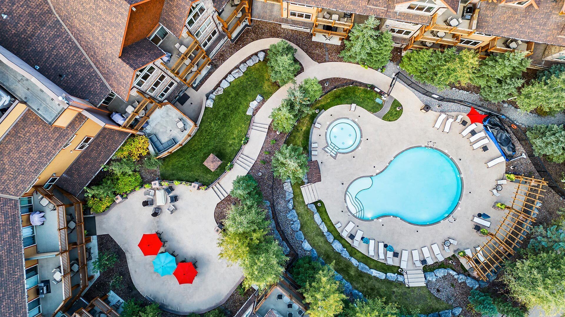 An aerial view of a resort with a central swimming pool, outdoor seating areas, and a landscaped garden.