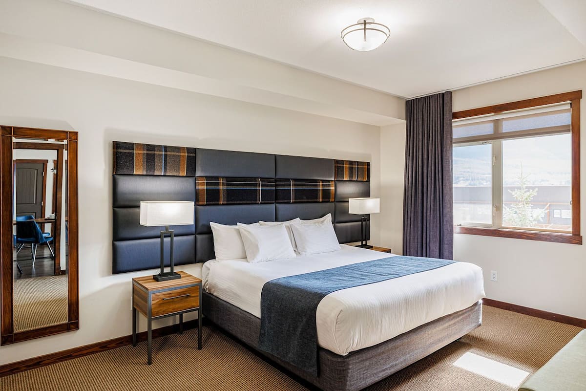 A hotel room with a large bed, two bedside tables, a mirror, and a window with curtains.