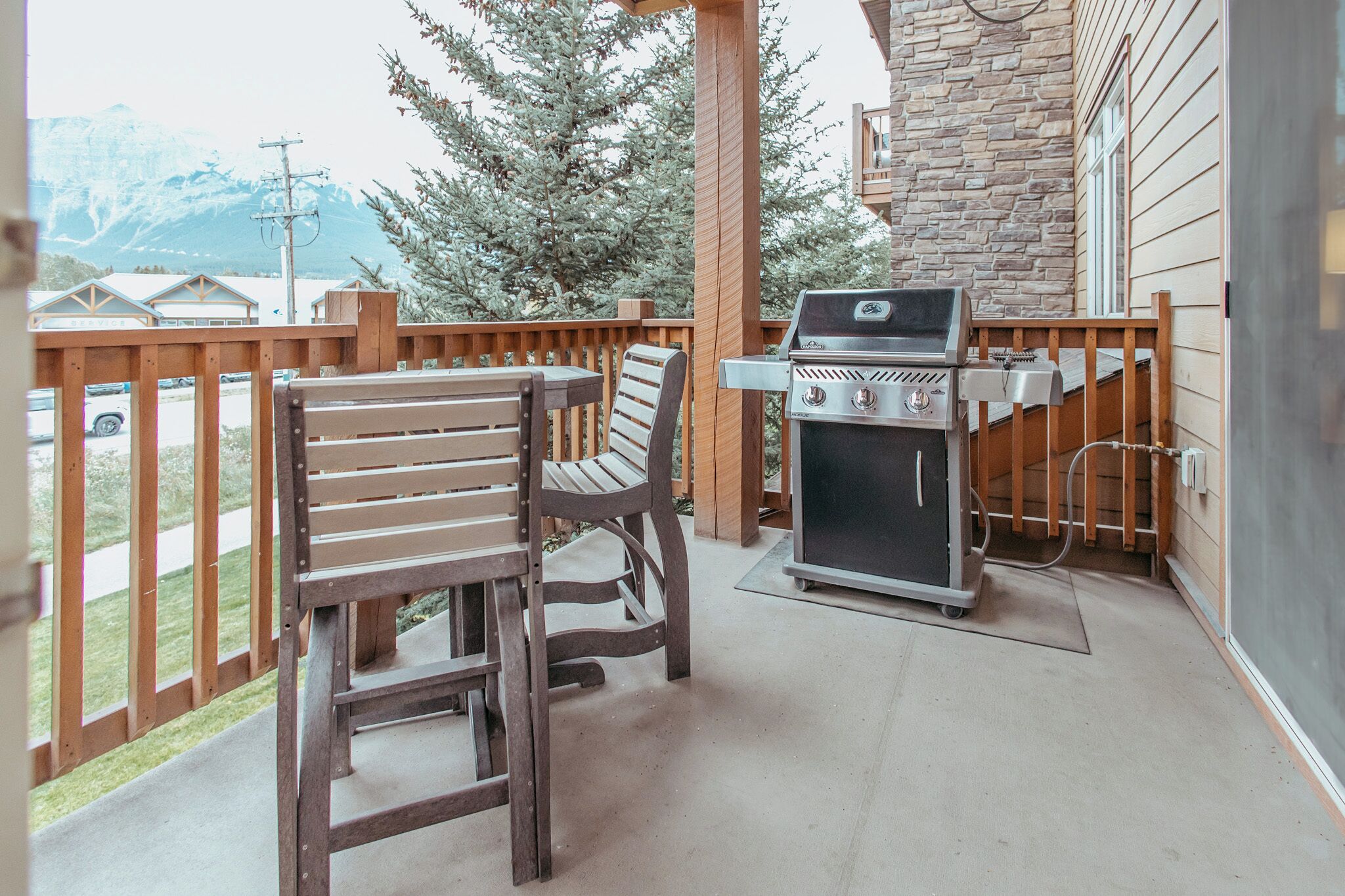 A patio with a grill, two wooden chairs, and a view of a mountain.