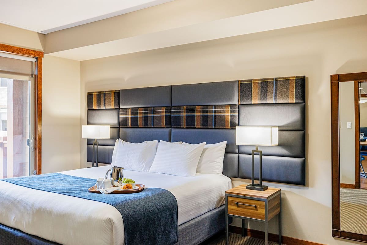 A hotel room with a large bed, a wooden nightstand, a mirror, and a view of the outside.