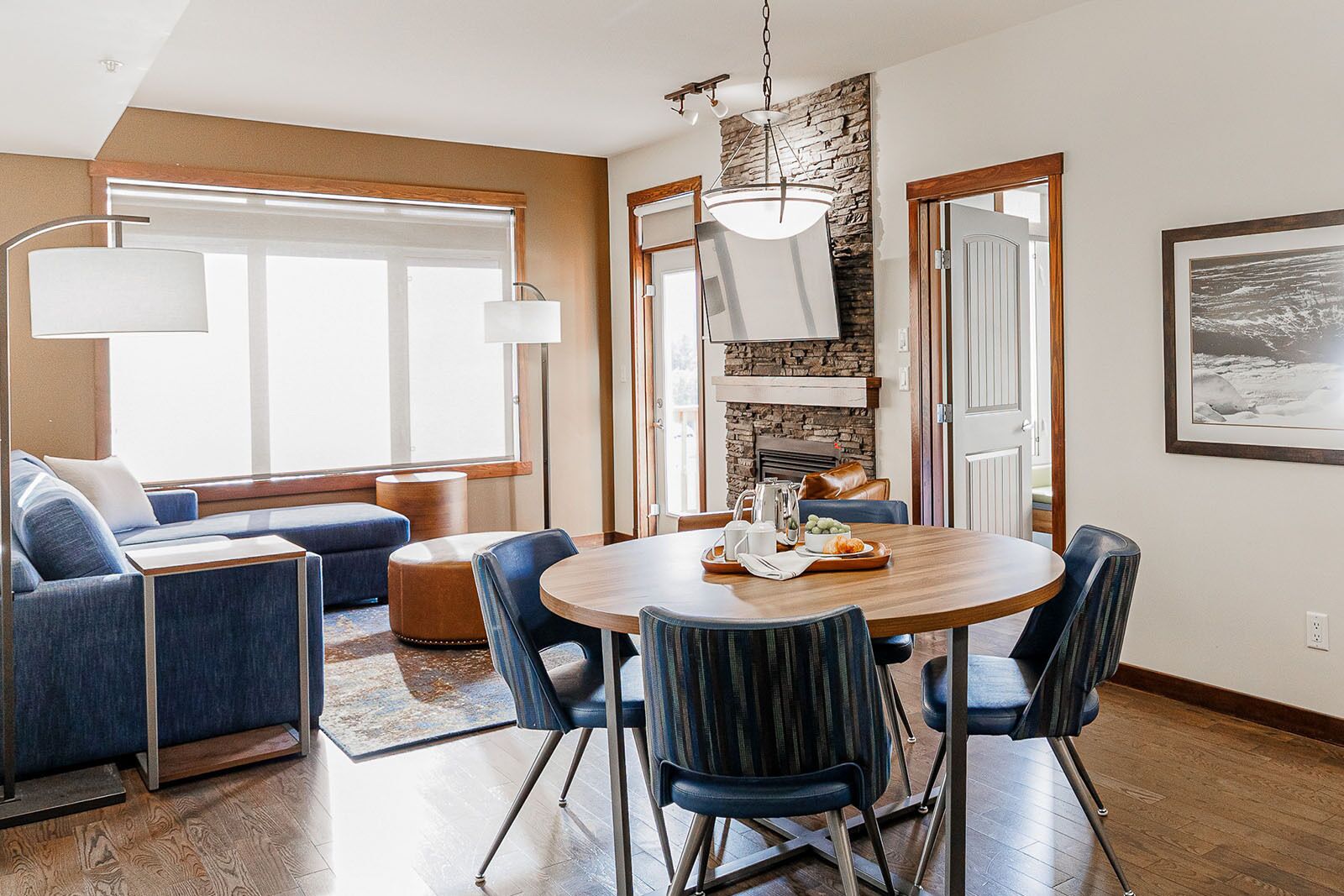 A modern dining area with a round wooden table, blue upholstered chairs, and a stone accent wall.