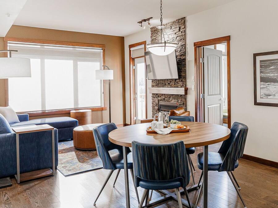 A modern dining area with a round wooden table, blue upholstered chairs, and a stone accent wall.