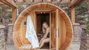 A wooden sauna with a bench and a towel rack, set in a stone and wood structure. - Stoneridge Mountain Resort (Canmore)