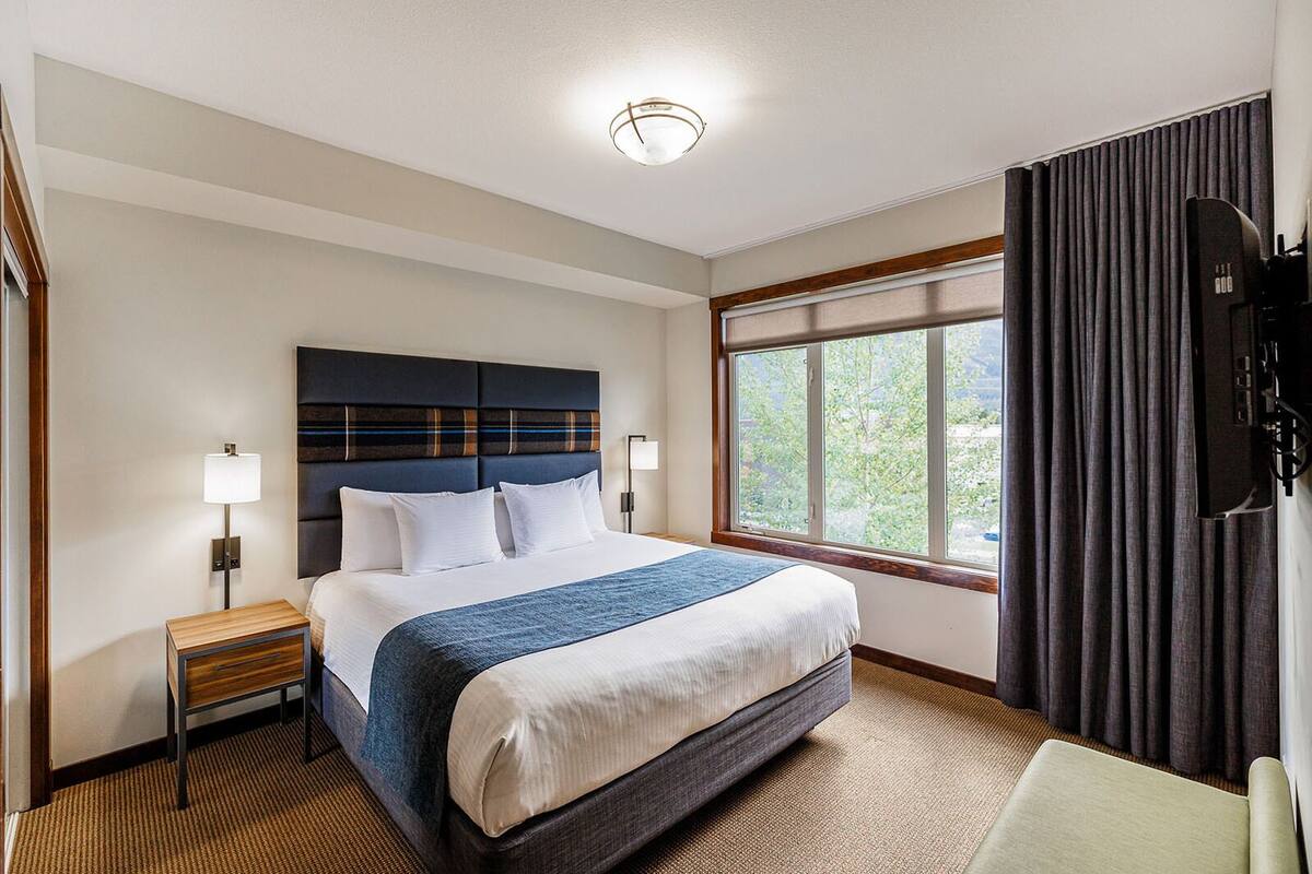 A hotel room with a large bed, a nightstand, a TV, and a window with curtains.