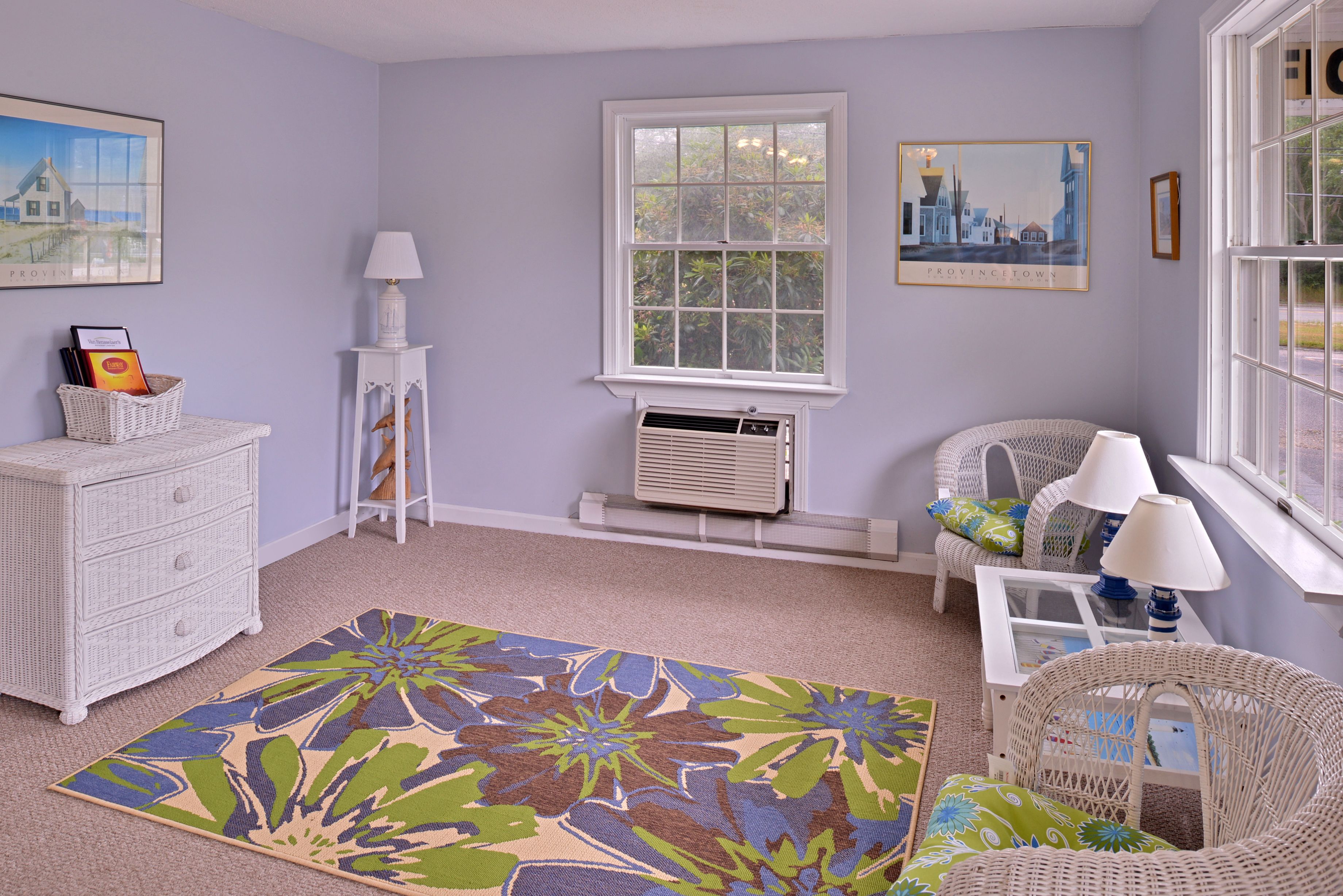 A room with a white dresser, wicker furniture, a floral rug, and two framed pictures on the wall.