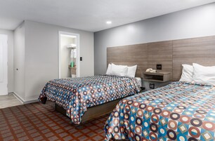 A hotel room with two beds, a wooden headboard, a nightstand, and a small shelf with toiletries.