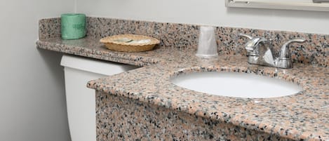 A bathroom with a granite countertop, a white sink, a towel rack with folded towels, a green towel dispenser, and a mirror.