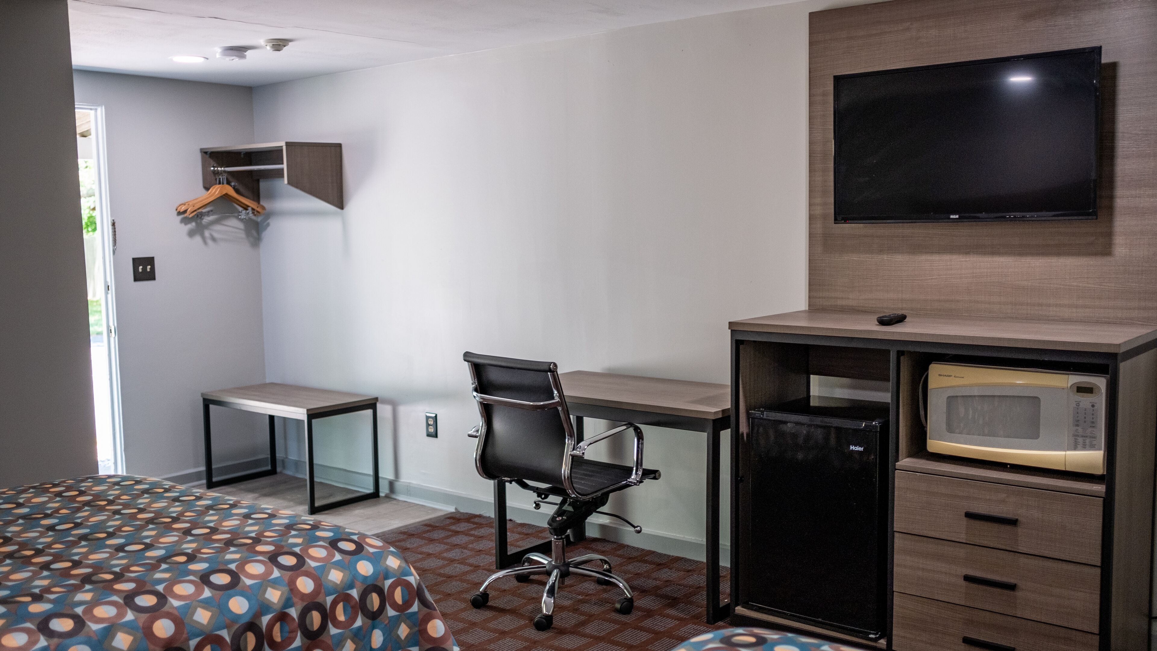 A hotel room with a bed, a desk, a chair, a television, and a microwave.