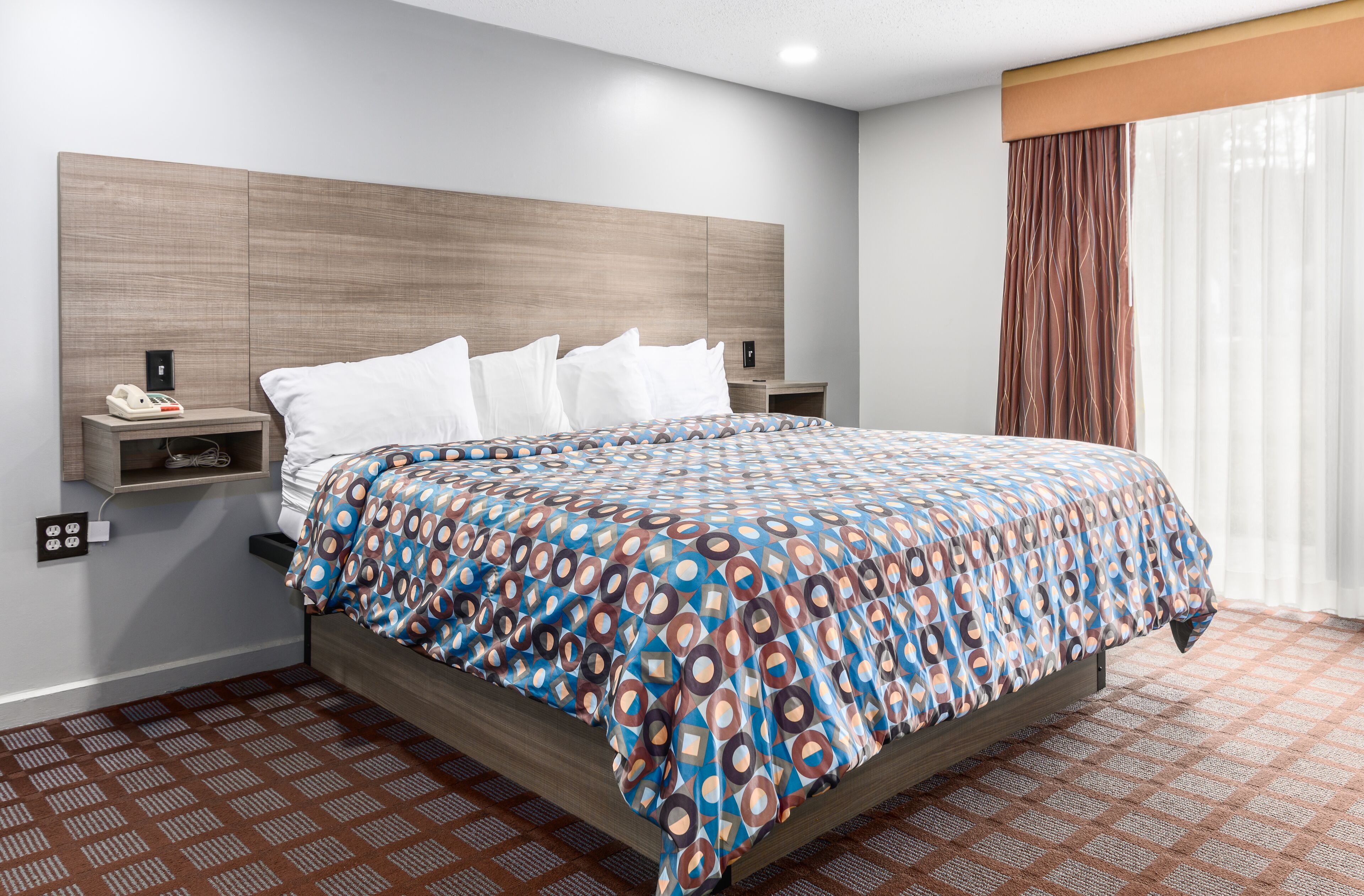 A hotel room with a bed, a nightstand, a phone, and a window with curtains.