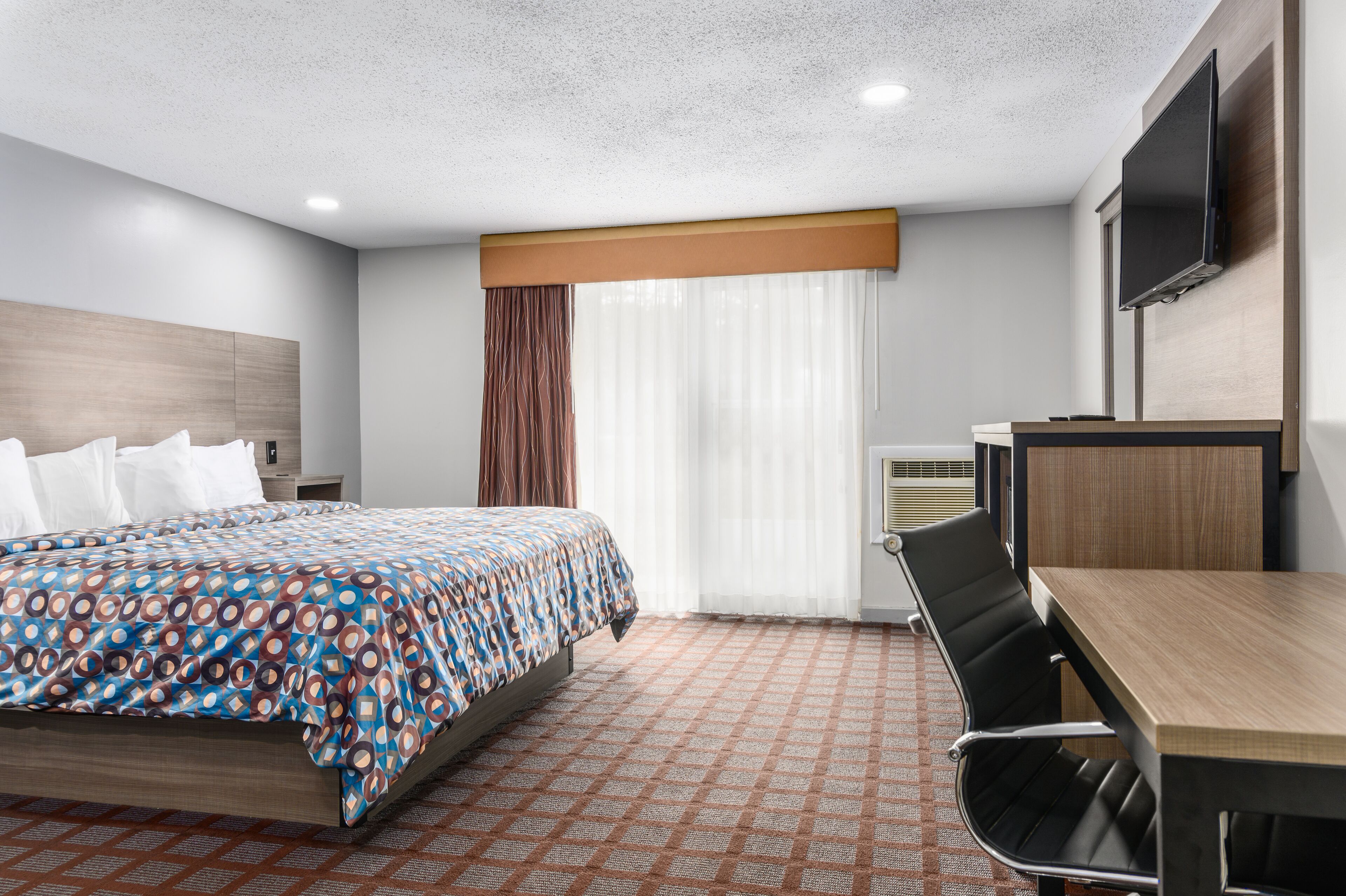 A hotel room with a bed, a desk, a chair, a TV, and a window with curtains.