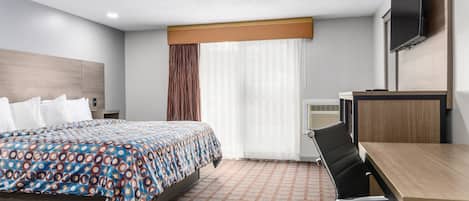 Habitación de hotel con cama, escritorio, silla, televisión y ventana con cortinas.