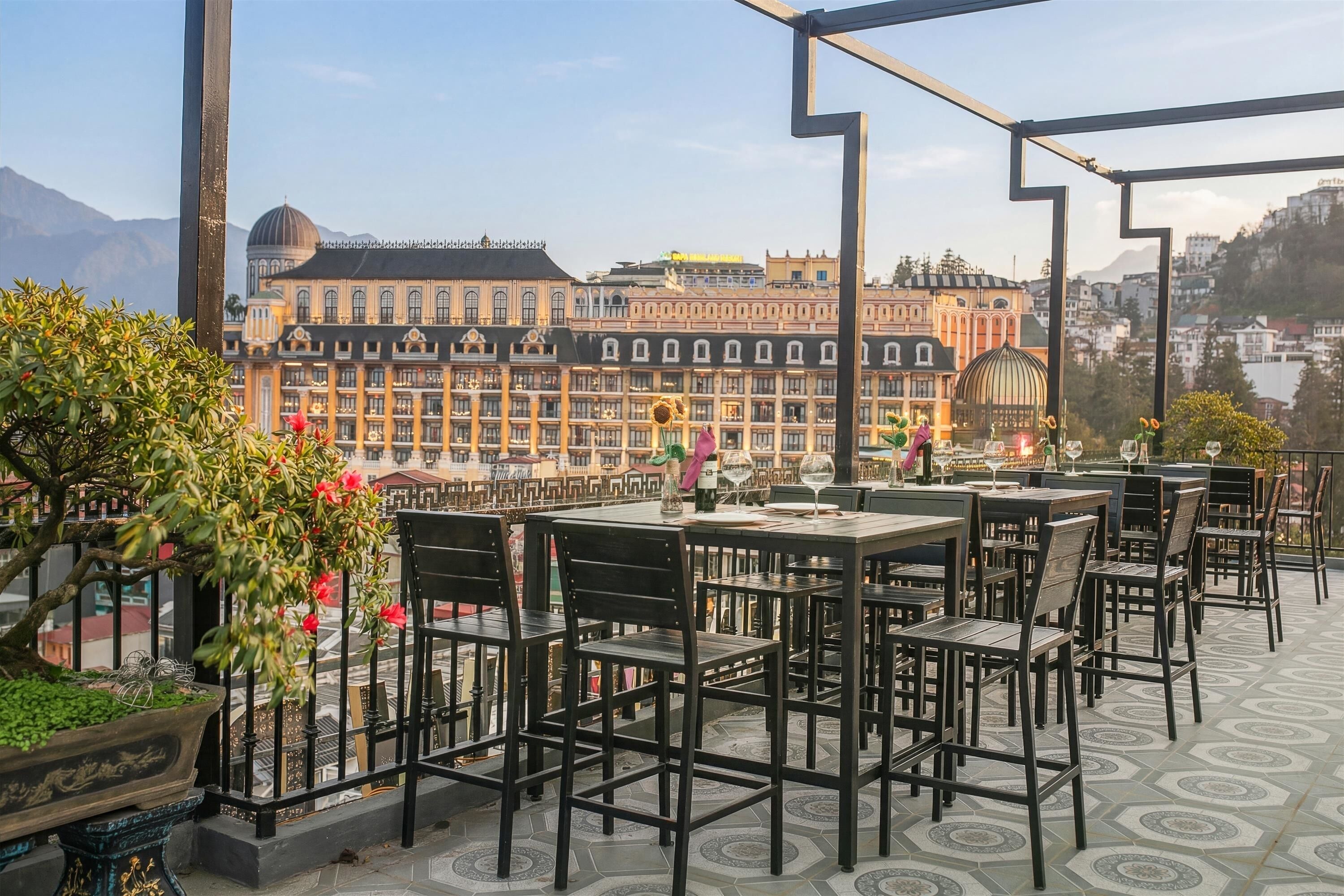 Una terraza al aire libre con mesas y sillas, una planta en maceta y vistas de un edificio histórico con múltiples ventanas y una cúpula.