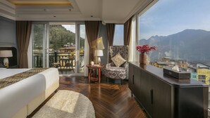 Habitación de hotel con una cama grande, una silla, una mesita y vistas a un paisaje montañoso.