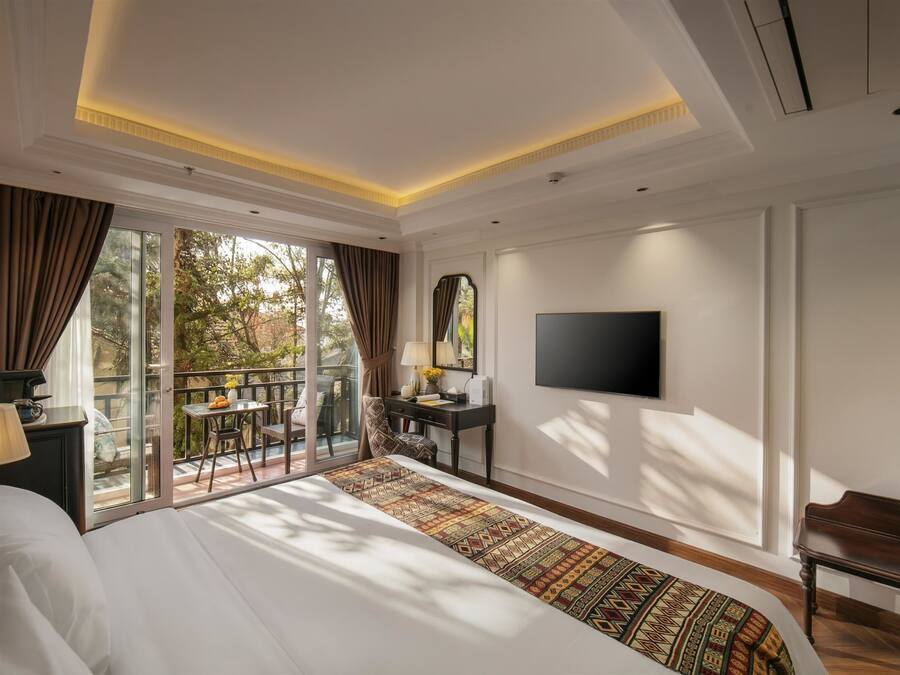 Ein Hotelzimmer mit einem großen Bett, einem an der Wand montierten Fernseher, einem Schreibtisch und einem Balkon mit Tisch und Stühlen.
