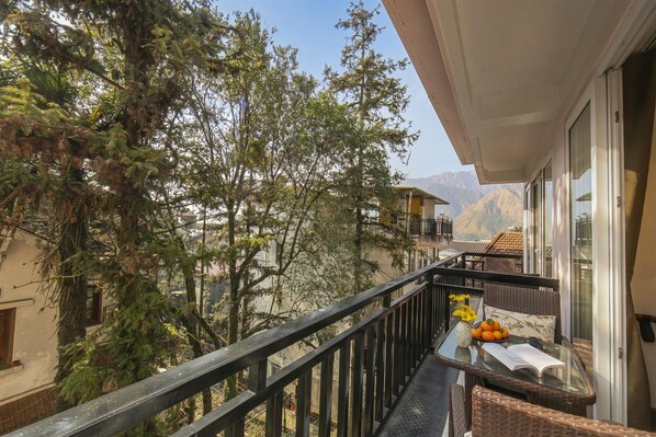 A balcony with a view of mountains, a table with a book and fruit, and a wicker chair.