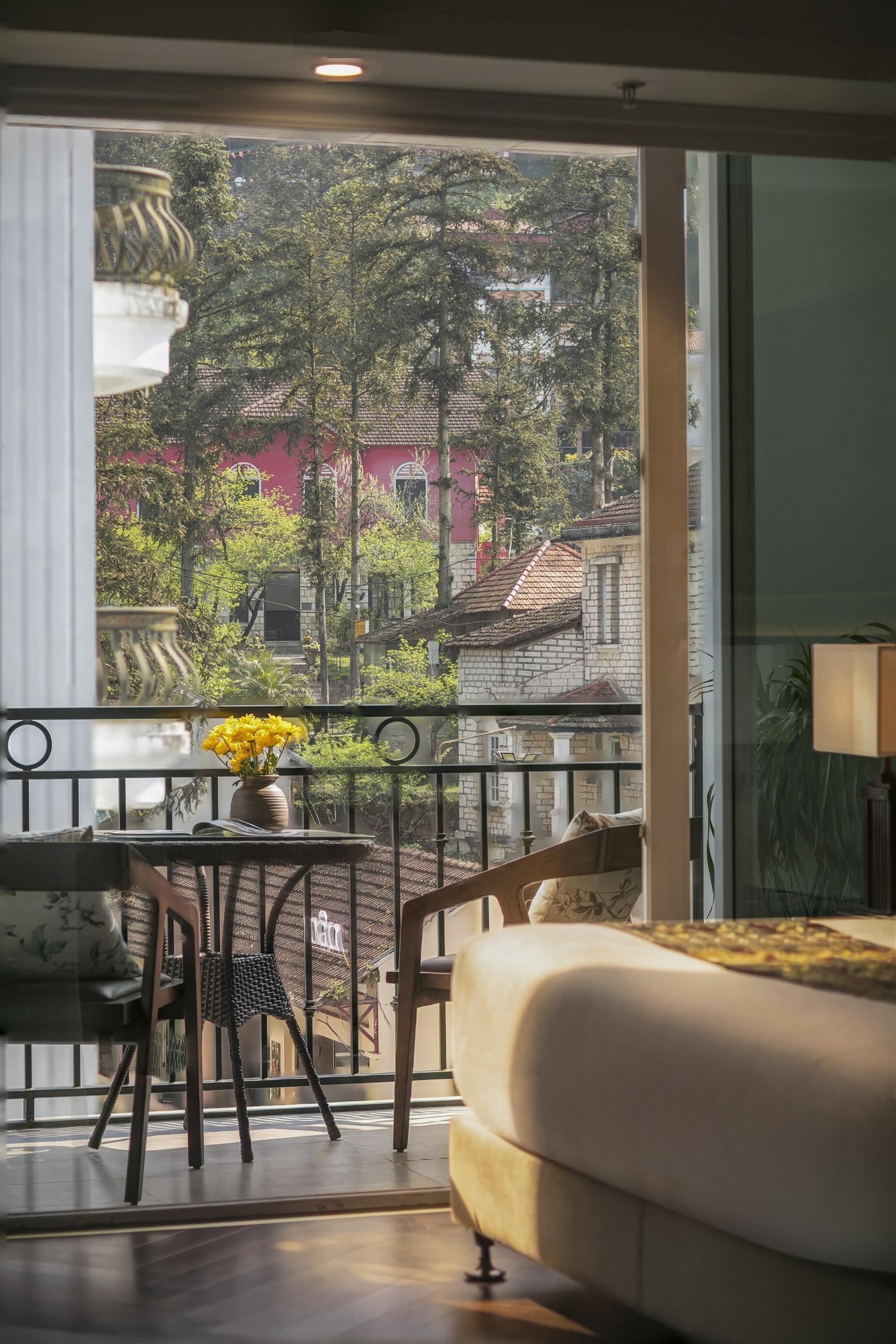 Un balcon donnant sur des immeubles et des arbres, une table avec un vase de fleurs et un canapé.