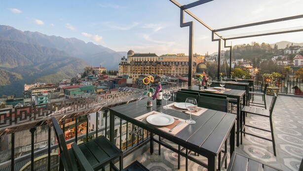 Un restaurante en la azotea con mesas dispuestas para comer, con vistas a un paisaje urbano y montañas.