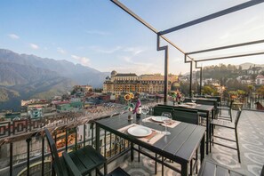 A rooftop restaurant with tables set for dining, overlooking a cityscape and mountains.