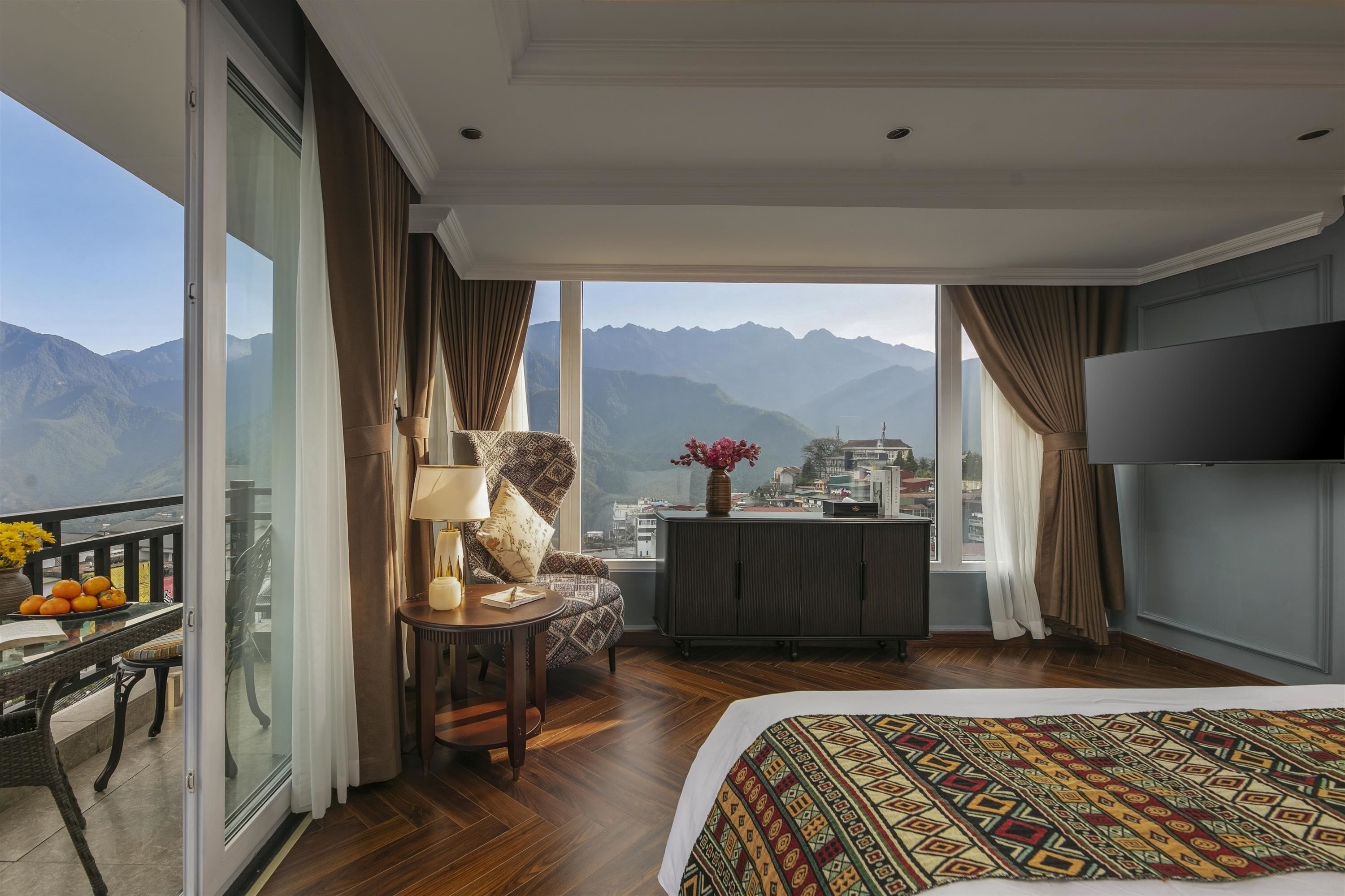 Camera d'albergo con un letto grande, una scrivania con lampada, una sedia, una televisione e vista sulle montagne.
