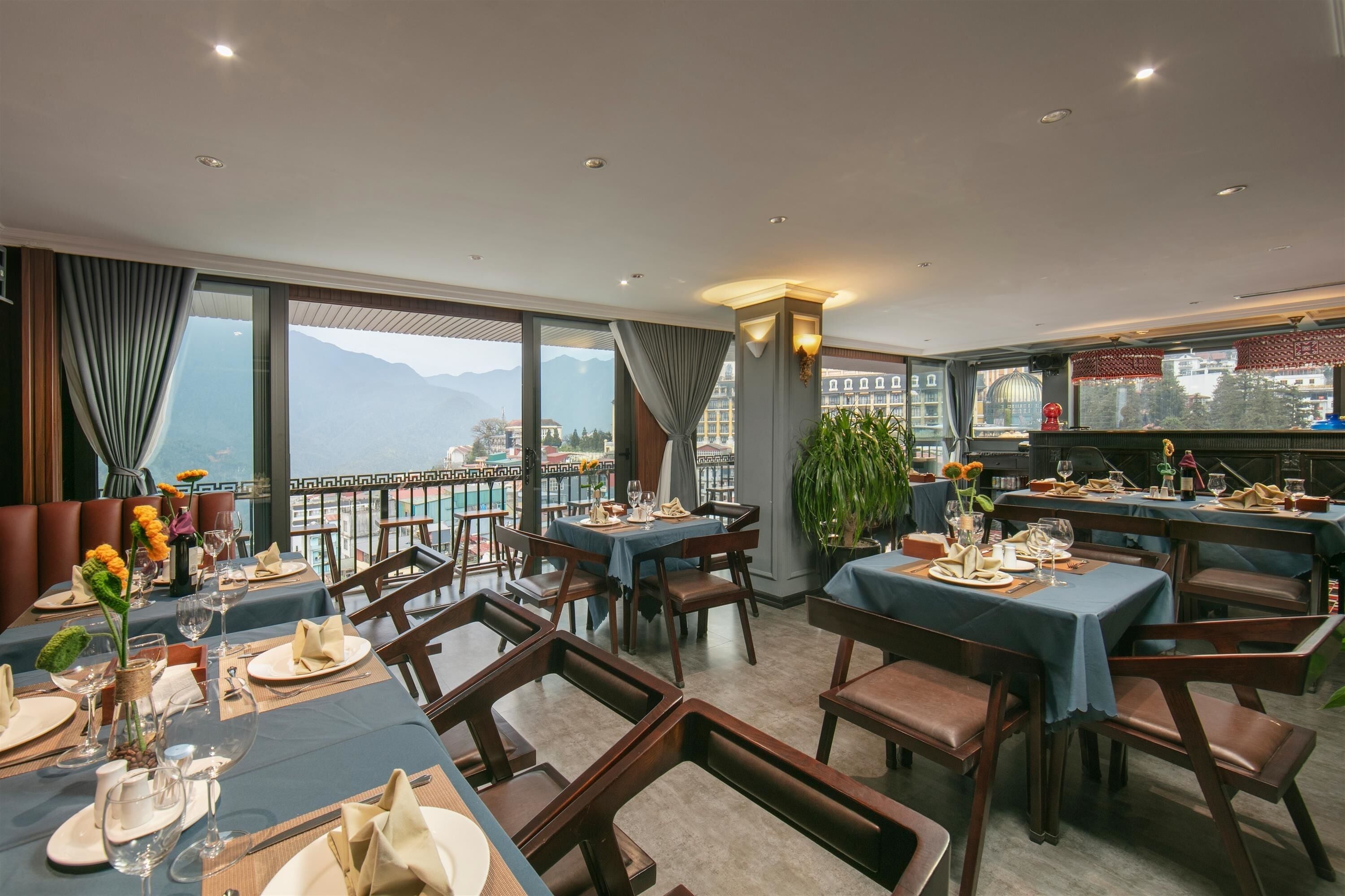 A restaurant with tables set for dining, large windows offering a view of mountains, and a balcony with a railing.