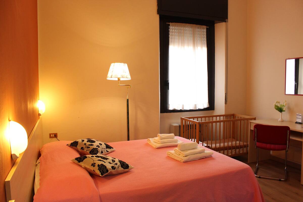 A hotel room with a bed, a crib, a desk, and a chair.