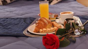Bandeja con cruasanes, un vaso de jugo de naranja, una taza de café y una rosa sobre la cama.