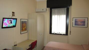A hotel room with a bed, a desk with a chair, a television, and a window with curtains.