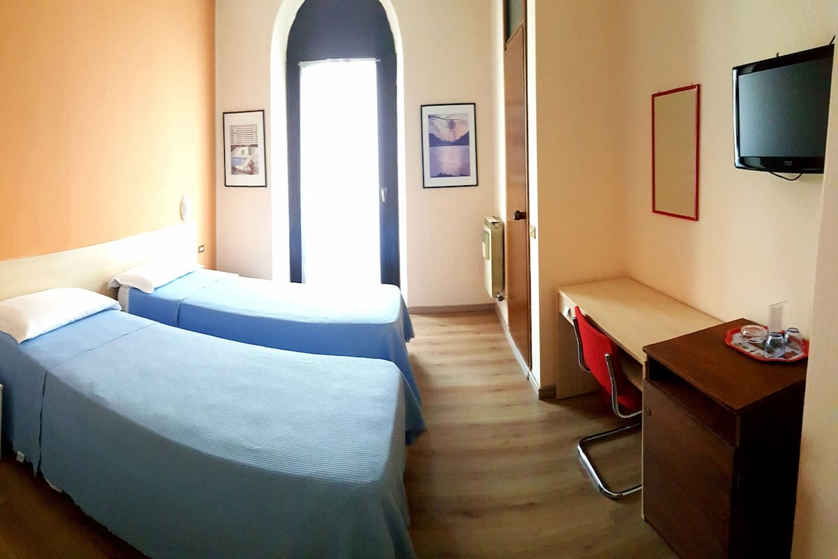 A hotel room with two beds, a desk, a TV, and a door leading to a corridor.