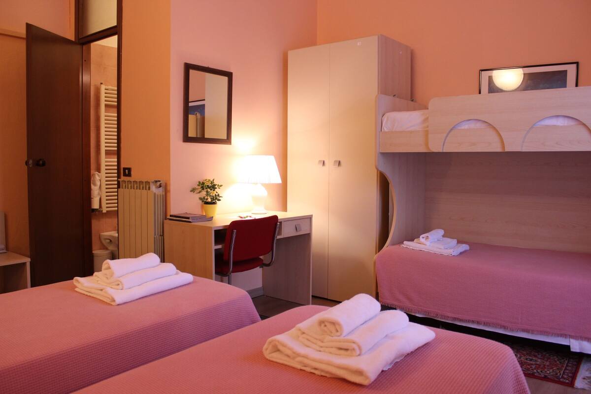 A hotel room with two beds, a desk, a chair, a wardrobe, and a bathroom visible through an open door.