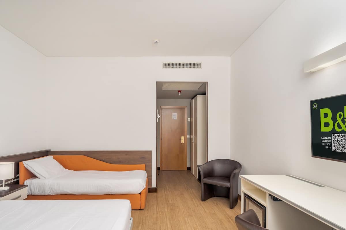 A hotel room with two beds, a desk, a chair, a wardrobe, and a wall-mounted sign.