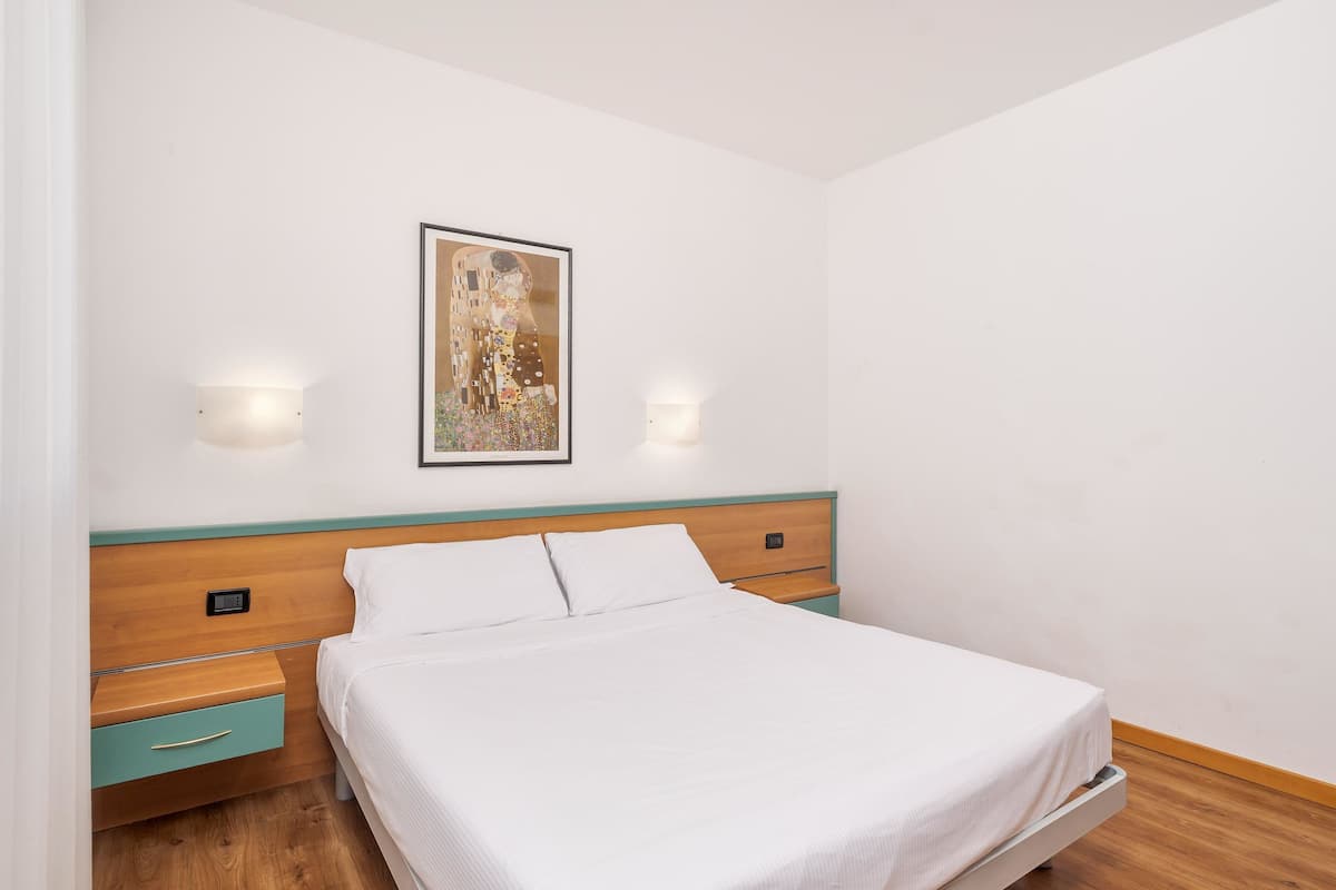 A neatly made bed with a wooden headboard, a bedside table with a drawer, and a wall-mounted light fixture.