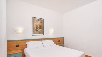 A neatly made bed with a wooden headboard, a bedside table with a drawer, and a wall-mounted light fixture.