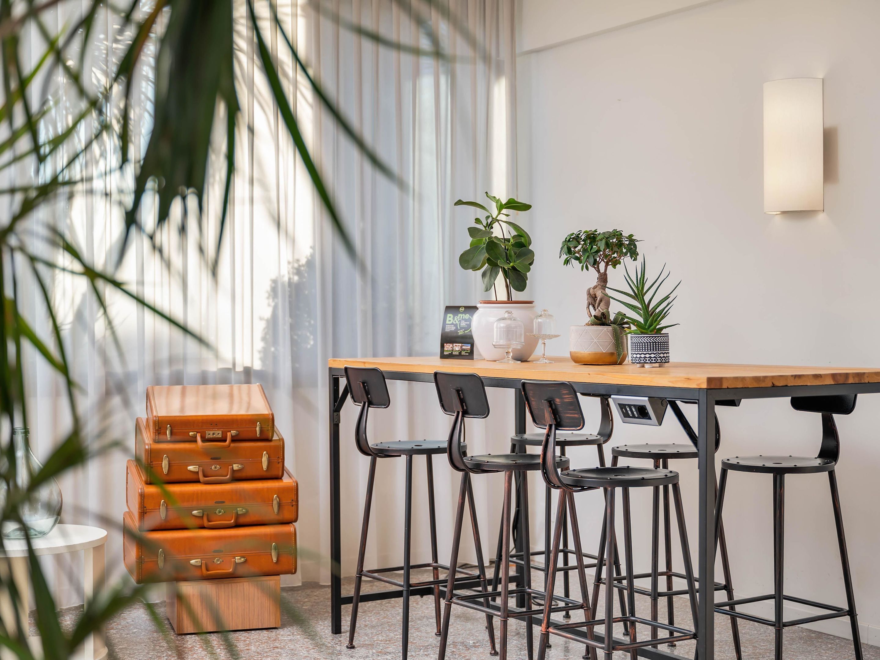 A modern room with a wooden table and metal bar stools, a potted plant, and vintage suitcases.