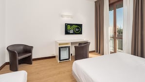 A hotel room with a bed, a desk, two chairs, a small fridge, and a TV on the wall. - B&B Hotel Eurorest Conegliano (Conegliano)