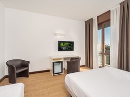 Habitación de hotel con cama, escritorio, dos sillas, un refrigerador pequeño y un televisor en la pared.