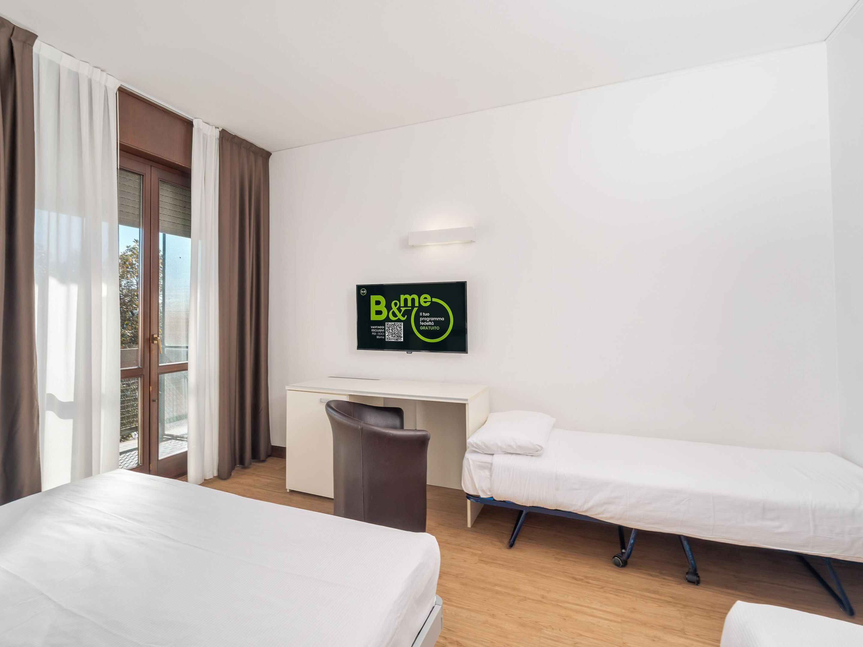 A hotel room with two beds, a desk, a chair, and a TV displaying a sign.