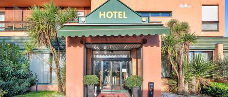 Entrada de un hotel con toldo verde, puerta de cristal y un cartel que dice 'HOTEL'.