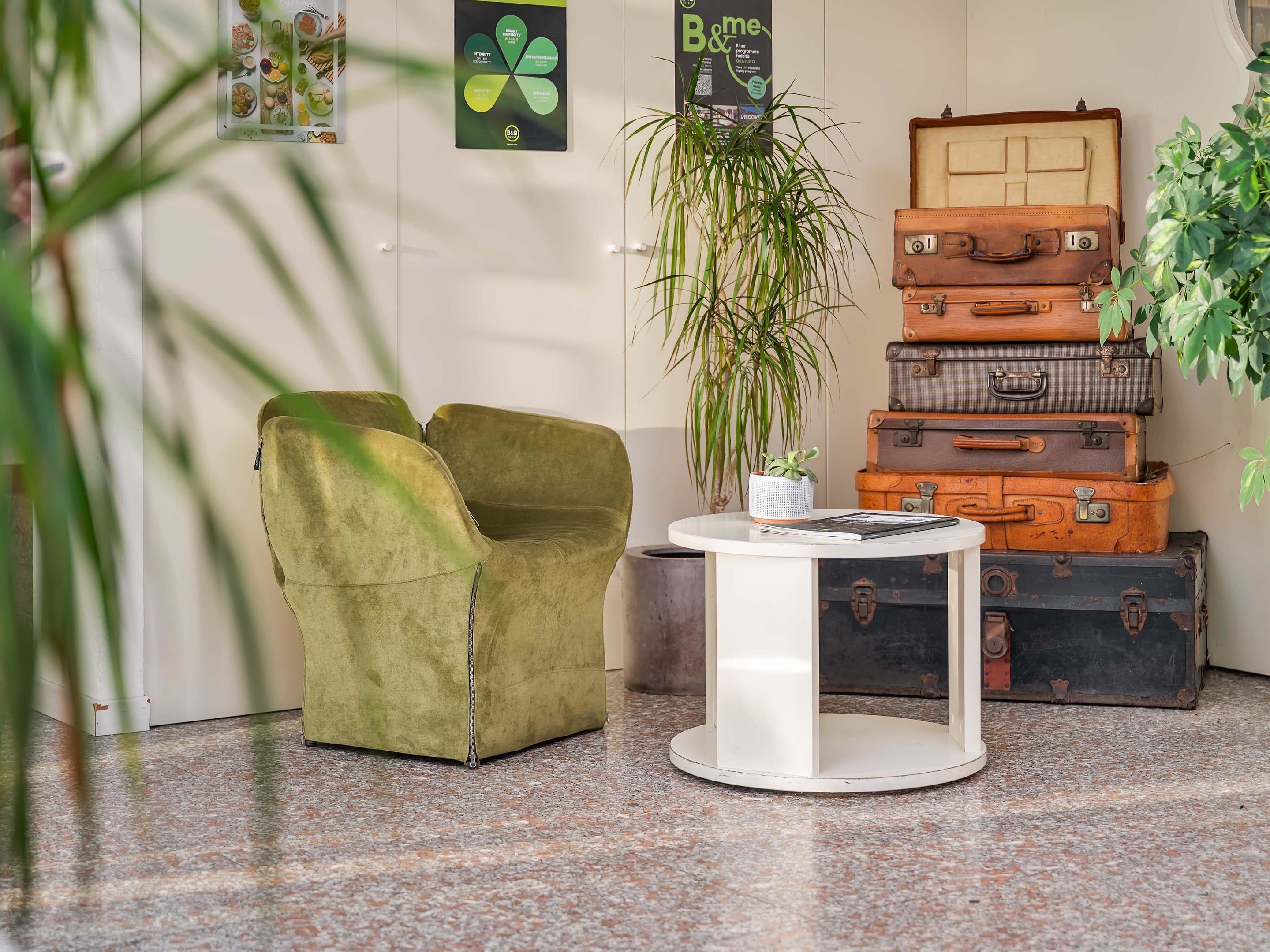 Un hall d’entrée avec un fauteuil vert, une table blanche ornée d’une plante et des valises empilées.