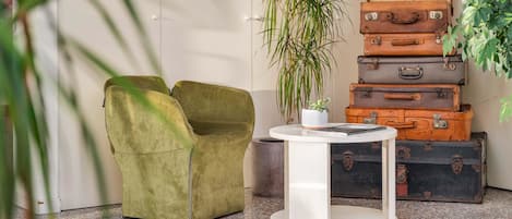 A lobby with a green armchair, a white table with a plant, and stacked suitcases.