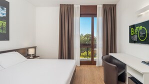 A hotel room with a bed, desk, and a view of the outdoors through a large window. - B&B Hotel Eurorest Conegliano (Conegliano)